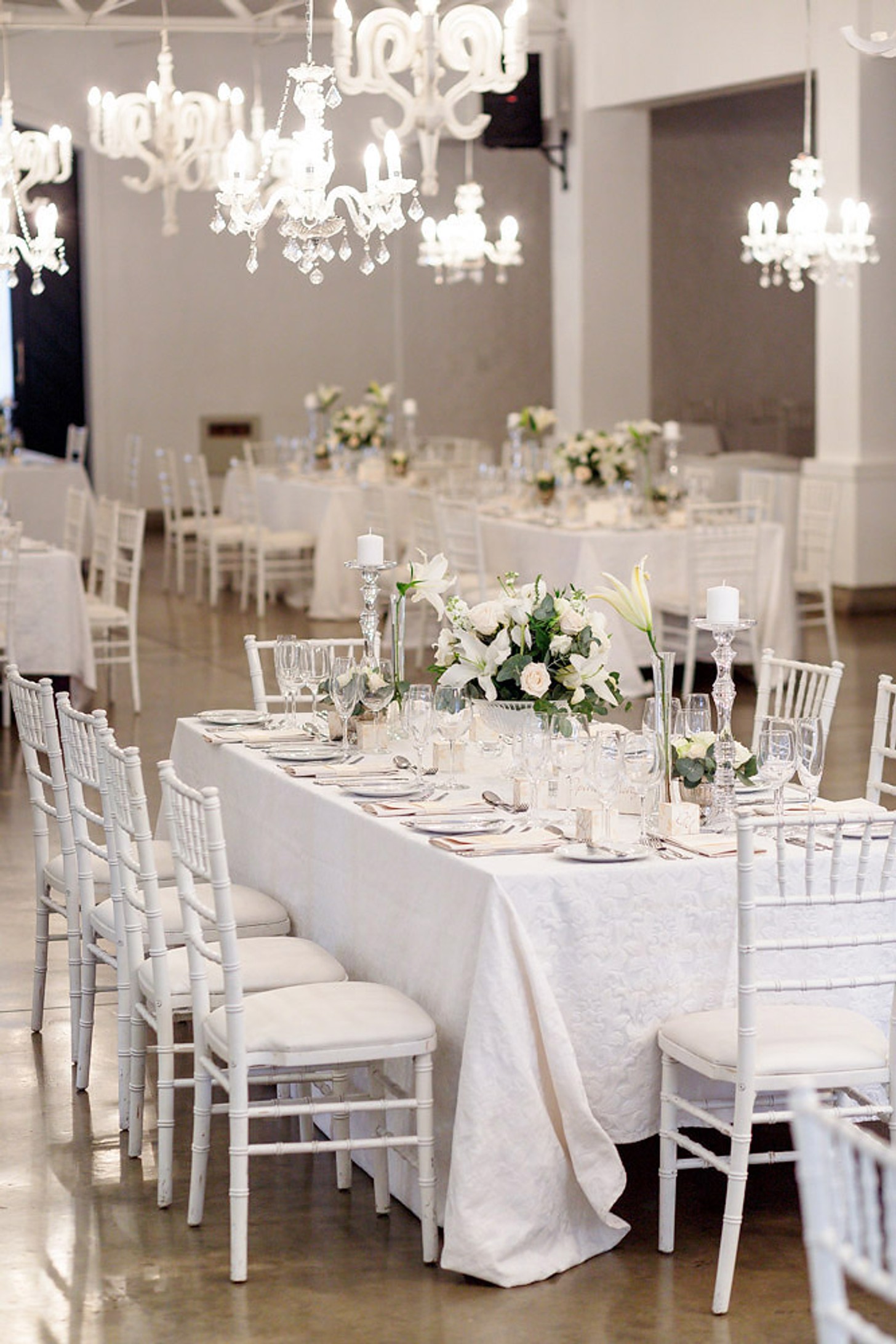 Elegant events decor setup with white floral centerpieces, gold-rimmed plates, & soft candlelight.